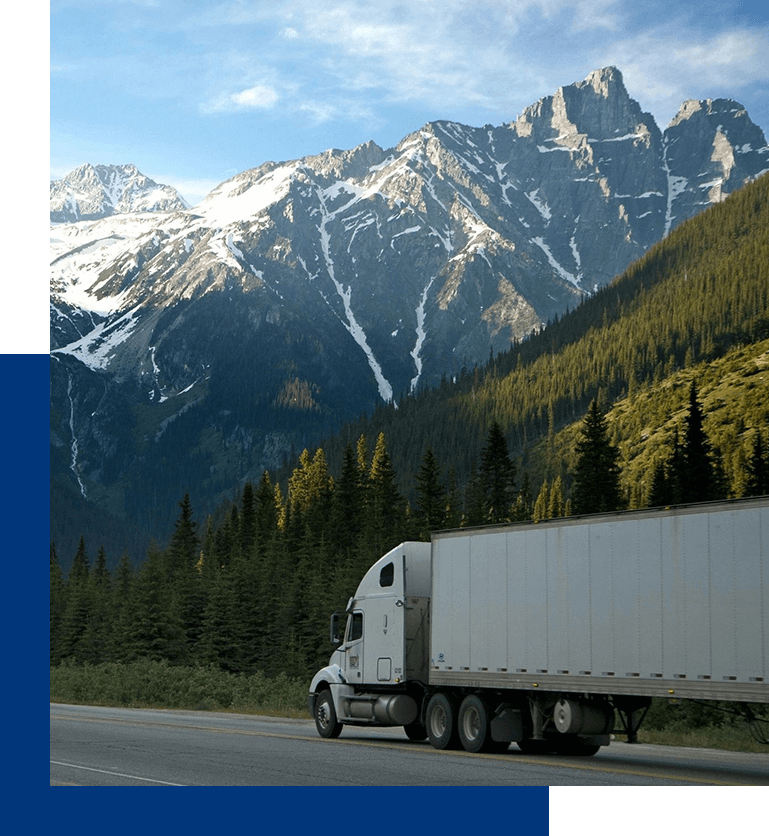 A truck driving down the road with mountains in the background.