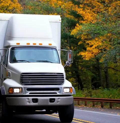 A white truck driving down the road near trees.